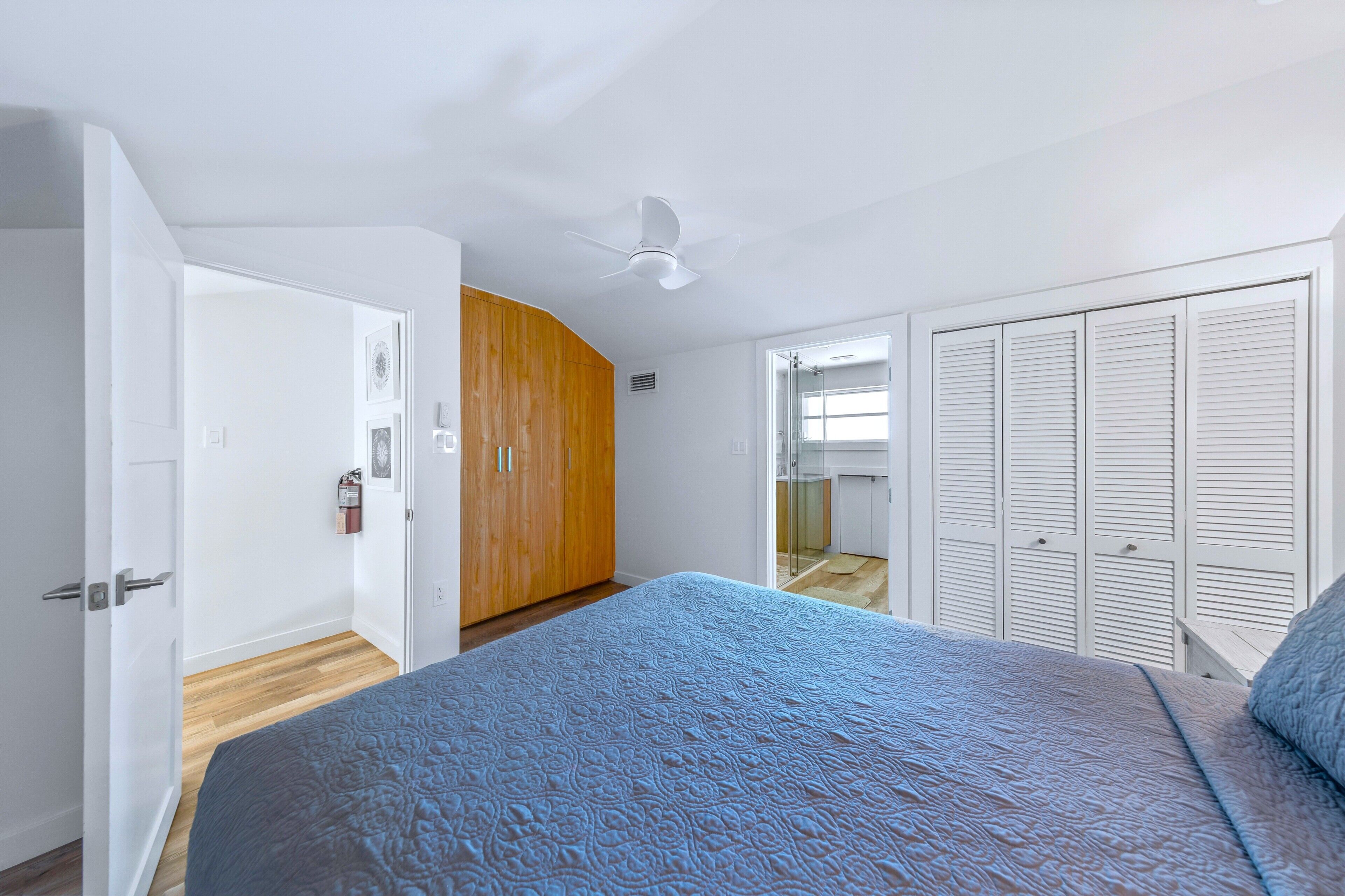Ein Schlafzimmer mit Bett, Deckenventilator, Kleiderschrank und einer Tür zu einem anderen Raum.