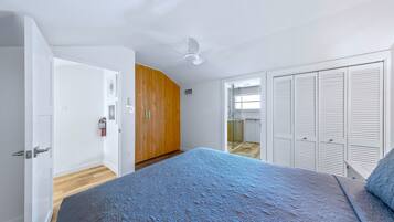 Ein Schlafzimmer mit Bett, Deckenventilator, Kleiderschrank und einer Tür zu einem anderen Raum.