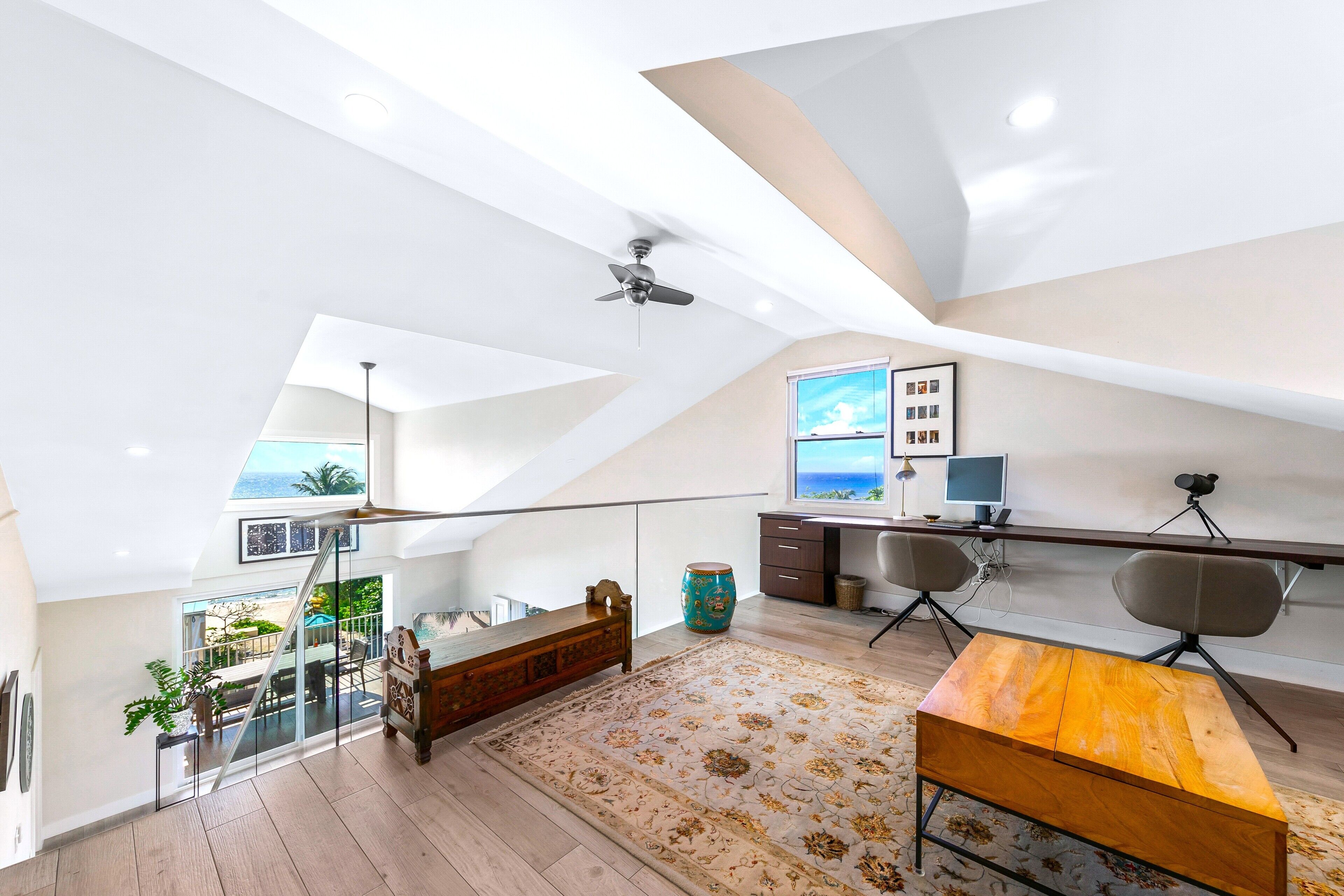Un loft espacioso con techo alto, ventilador de techo, ventana grande con vistas, escritorio con computadora y zona de comedor.