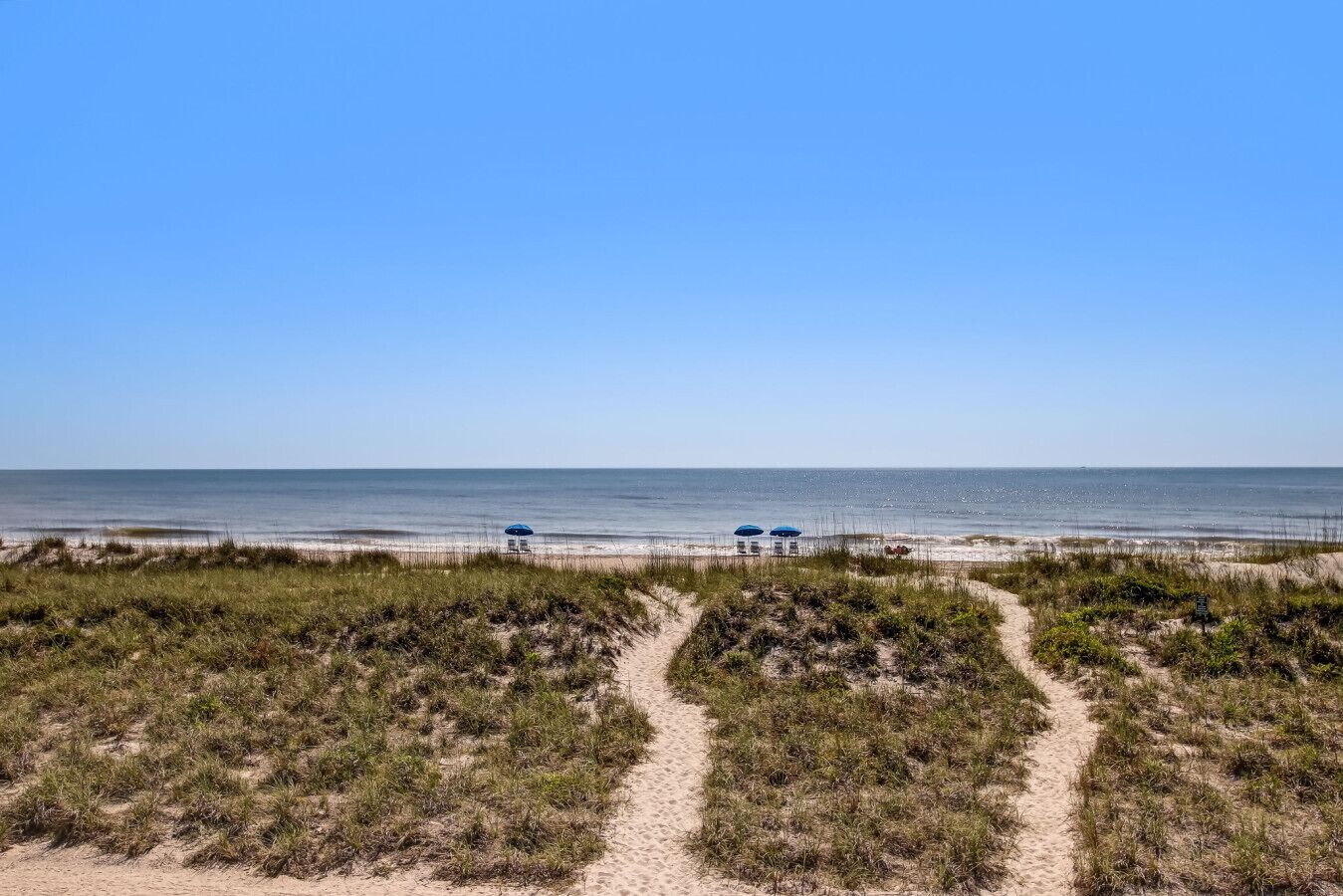 A beach with a clear sky, sandy paths, and two umbrellas.
