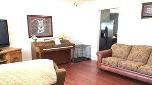 Una sala de estar con un piano, un televisor, un sofá y un cuadro en la pared.