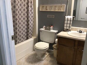 Et badeværelse med toilet, håndvask, spejl, badeforhæng og et skilt på væggen.
