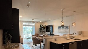 A modern kitchen with a central island, dark cabinetry, and pendant lighting. - NEW Designer Coastal Condo - Sleeps 8 -Close to Downtown Rehoboth Next to Dining (Rehoboth Beach)