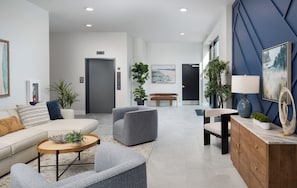 Un salon moderne comprenant un canapé, des fauteuils, une table basse et un coin repas avec une table et un banc. On y trouve également des plantes en pot, des œuvres d’art accrochées aux murs et un mur d’accent de couleur bleue.