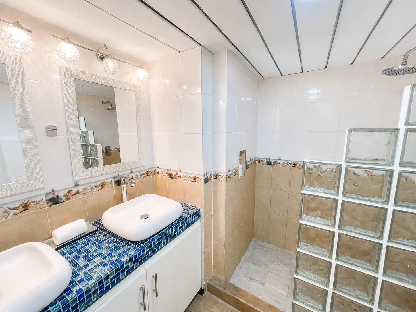A bathroom with a white sink, a mirror, a shower, and a tiled floor.