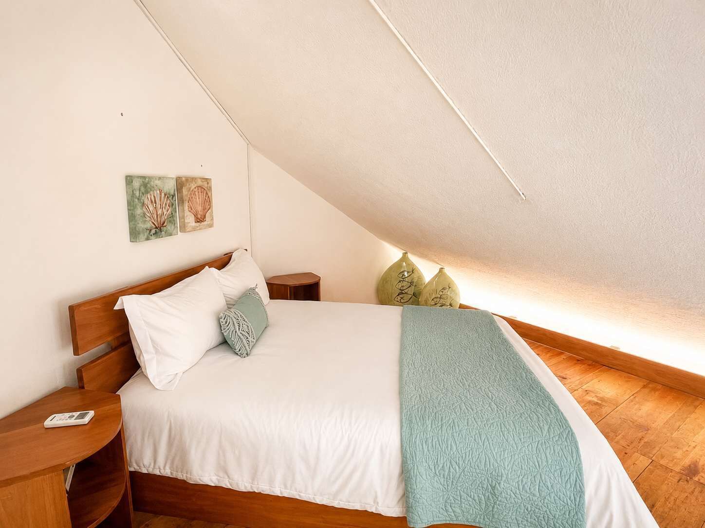 Ein Schlafzimmer mit schrägen Wänden, einem hölzernen Bettgestell, weißer Bettwäsche und zwei Nachttischen.