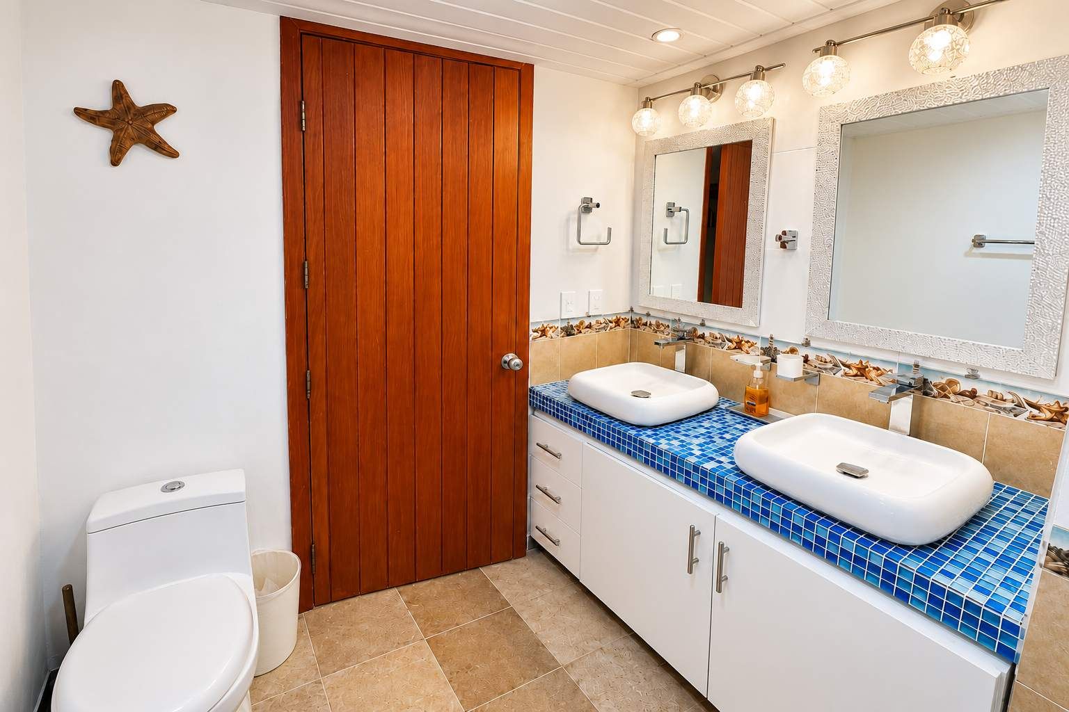 Ein Badezimmer mit Holztür, zwei Waschbecken, einem Spiegel und einer Meerstern-Dekoration.