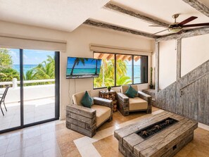 A spacious living area with a large TV, wooden furniture, and a view of the ocean.