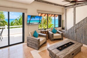 Un amplio salón con televisor grande, muebles de madera y vista al océano.