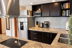 A modern kitchen with stainless steel appliances, a granite countertop, dark cabinetry, and a backsplash. - Beachfront condo with loft and sea views (Puerto Aventuras)