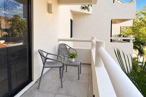 Un balcon avec deux chaises et une petite table, un pot de fleurs et une vue sur la verdure.