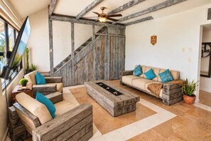 Ein Wohnzimmer mit einer Holztreppe, einem Deckenventilator, einem Flachbildfernseher und einer Couch mit Kissen.