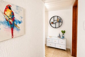 Un pasillo con una pared blanca texturizada, un armario blanco con tiradores dorados y un estante redondo negro con libros y una planta.