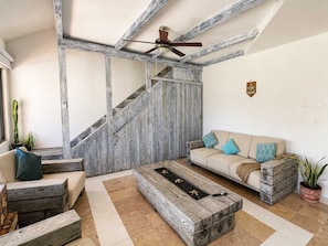 A living room with a staircase, a sofa, a coffee table, and a ceiling fan. - Beachfront condo with loft and sea views (Puerto Aventuras)