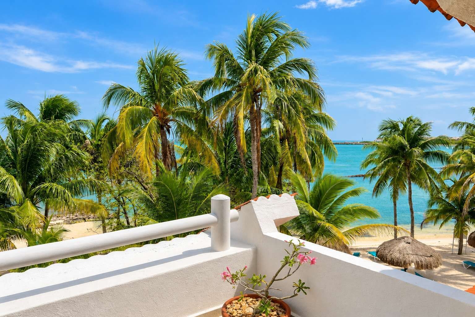 A balcony with a view of a beach, palm trees, and a clear sky.