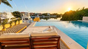 A poolside area with lounge chairs, a clear view of the water, and boats in the background. - Canal view, pool, 7-min walk to beach (Puerto Aventuras)