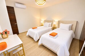 Quarto de hotel com duas camas, uma escrivaninha, uma cadeira, uma mesa com flores e um ar condicionado fixado na parede.