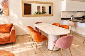 Cozinha moderna com armários brancos, bancada de mármore e área de jantar com mesa branca e cadeiras laranjas.