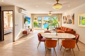 A modern hotel room with a dining area, a large window with a view of a pool, and a ceiling fan. - Canal view, pool, 7-min walk to beach (Puerto Aventuras)