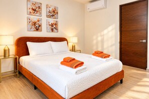 A hotel room with a large bed, two bedside lamps, a wooden door, and floral artwork on the wall. - Canal view, pool, 7-min walk to beach (Puerto Aventuras)