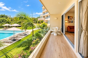 A balcony with a pool, outdoor furniture, and a view of a hotel building. - Canal view, pool, 7-min walk to beach (Puerto Aventuras)