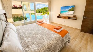 A bedroom with a large bed, a TV, a view of the pool, and a door to the outside. - Canal view, pool, 7-min walk to beach (Puerto Aventuras)