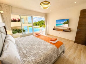 Une chambre avec un grand lit, une télévision, une vue sur la piscine et une porte donnant sur l’extérieur.