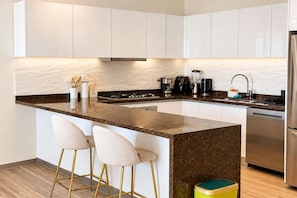 Una cocina moderna con armarios blancos, encimera de mármol, estufa a gas, cafetera y refrigerador de acero inoxidable.