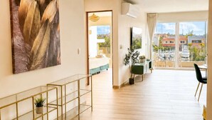 A spacious room with a large window, a view of the city, a modern kitchen area, and a dining space. - Canal View | 2 King Beds | 7 min to Beach (Puerto Aventuras)