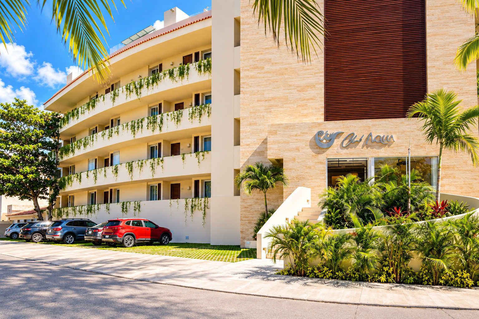 Un hotel de varios pisos con balcones, estacionamiento y un jardín bien cuidado.