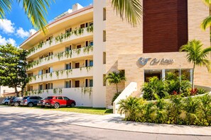 A multi-story hotel with balconies, a parking area, and a well-maintained garden. - Luxury 3BR Canal View Condo Near Beach (Puerto Aventuras)