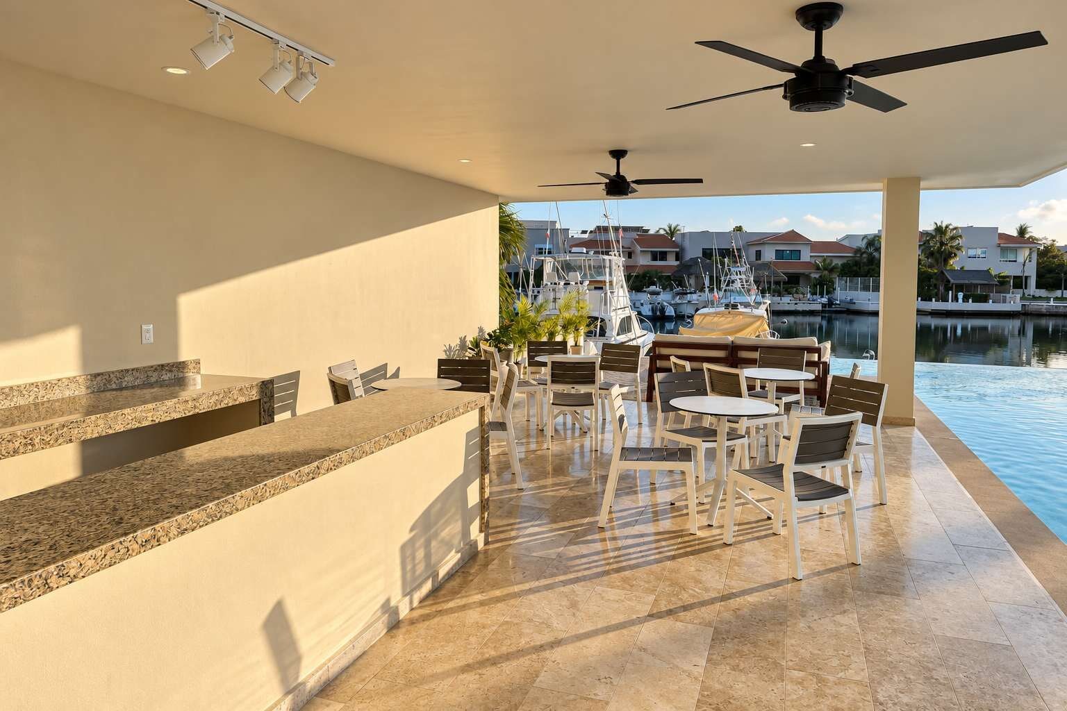 Un espace extérieur ensoleillé, aménagé avec des meubles de jardin, une piscine, des chaises et des tables, et offrant une vue sur un port de plaisance rempli de bateaux.