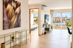 En rummelig opholdsstue med et stort vindue, et spiseområde med udsigt og et moderne design med et glasbord og en plante.