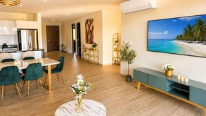 A modern living room with a dining area, a large flat-screen TV, and a kitchen in the background. - Canal View | 2 King Beds | 7 min to Beach (Puerto Aventuras)