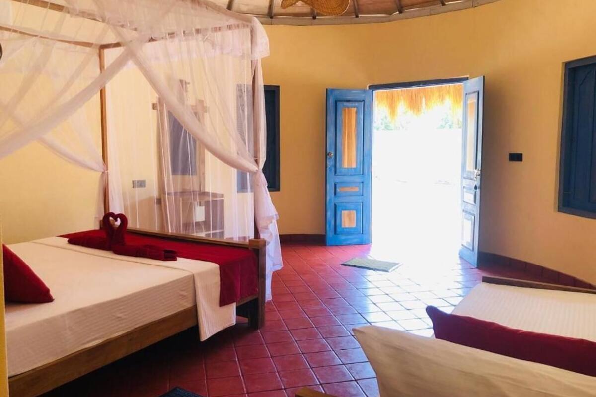 Una habitación con dos camas, un mosquitero y una puerta azul que da al exterior.