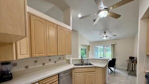 A kitchen with wooden cabinets, a dishwasher, a sink, a ceiling fan, and a dining area with a table and chairs. - Sunset Palms, lake view-Near manatees, golf & scalloping (Crystal River)