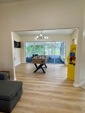 Ein geräumiges Zimmer mit Kicker, einer Couch und einem großen Fenster mit Blick ins Freie.