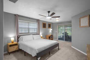 Un dormitorio con cama, mesitas de noche, un escritorio, una silla, un ventilador de techo y vistas al exterior.
