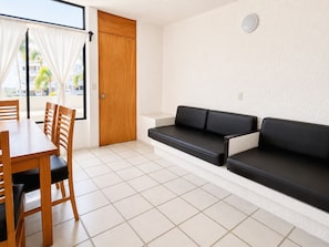 Una habitación con una mesa de comedor, sillas, un sofá negro, una puerta de madera y vistas a través de una ventana.