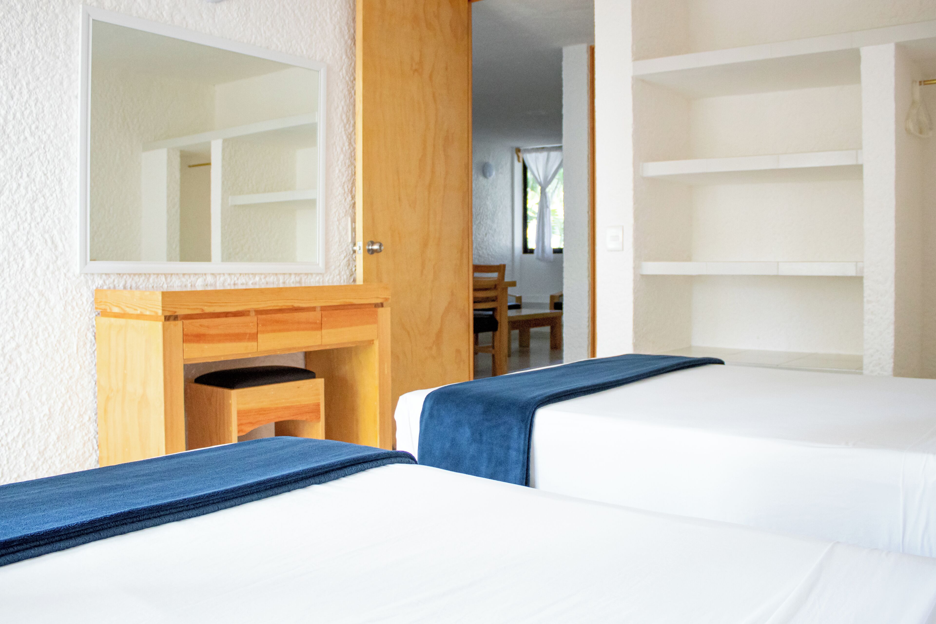 Una habitación con dos camas, un escritorio de madera, un espejo y una silla.