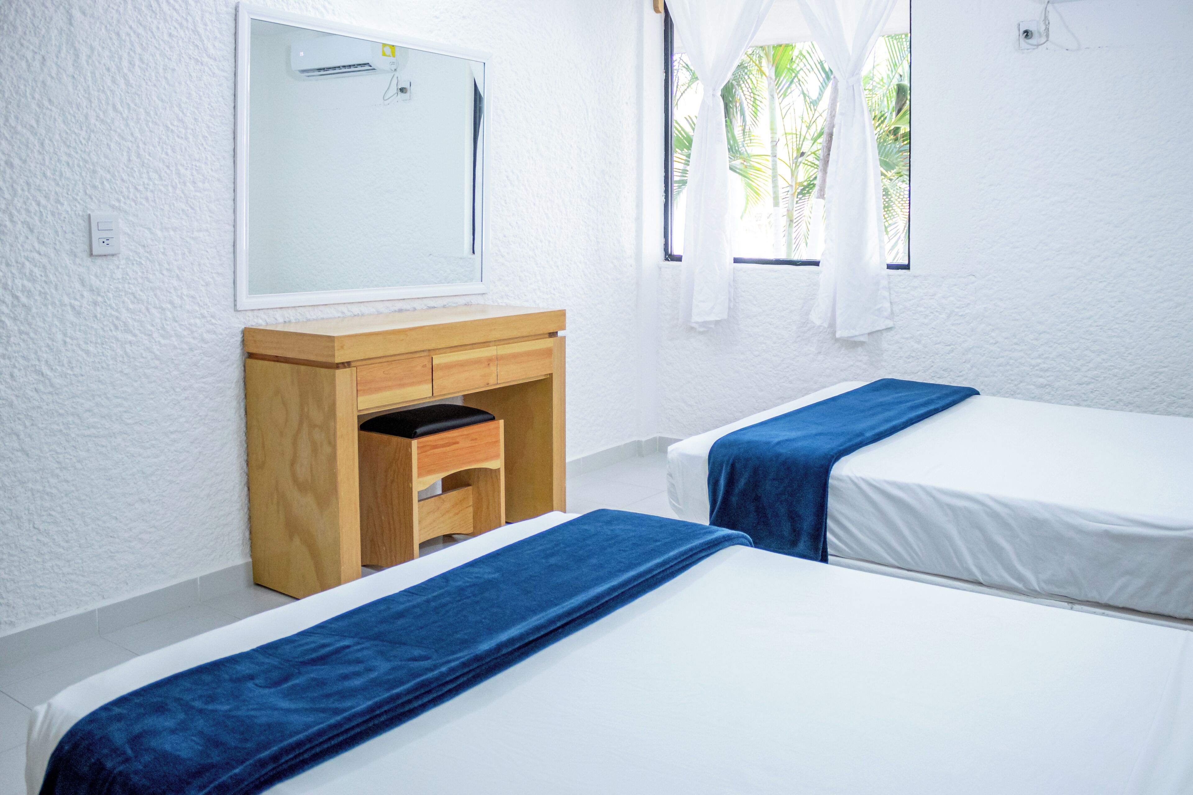 Habitació amb dos llits, un armari de fusta, un mirall i una finestra amb cortines.
