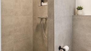 A modern bathroom with a walk-in shower, a toilet, and a small shelf with toiletries. - Comfortable Premium Business Apartment Darmstadt-Griesheim Including parking space (Griesheim)