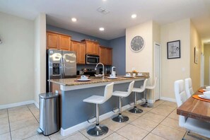 A modern kitchen with a central island, bar stools, and a dining table. - Storey Lake 5BR | Private Pool | Resort Water Park | Near Disney (Kissimmee)