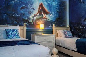 Un dormitorio con dos camas, una mesita de noche y un mural con una sirena.