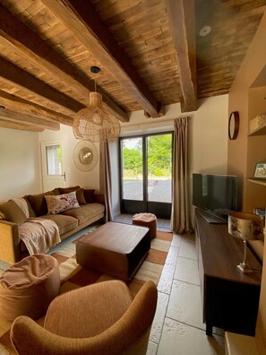 A cozy living room with a sofa, ottoman, and a TV. - Gîte Kerbremon (Elven)