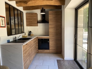 A modern kitchen with wooden cabinetry, a built-in oven, and a large window. - Gîte Kerbremon (Elven)