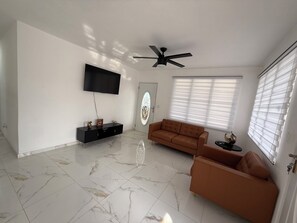 Una sala de estar con televisor de pantalla plana, ventilador de techo, sofá y mesa de centro.