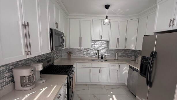 Una cocina moderna con armarios blancos, un refrigerador de acero inoxidable, una cafetera y un microondas.
