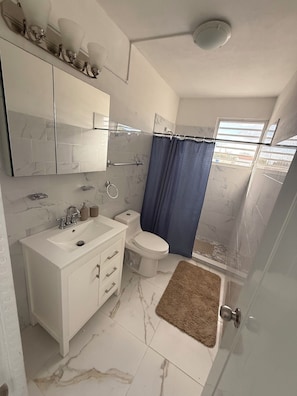 Un baño con lavamanos, inodoro y zona de ducha blancos.
