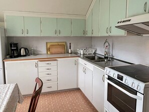 A compact kitchen with white cabinets, a stove, a sink, and a wooden cutting board. - 5 Person Holiday Home in Emmaboda (Emmaboda)